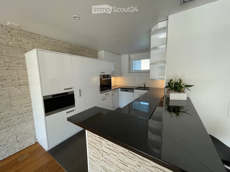 Modern kitchen with white cabinets, black countertops, built-in oven, and a stone accent wall.