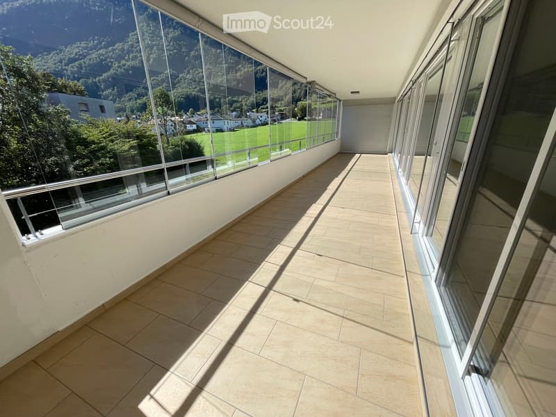 Spacious balcony with large glass windows, tiled floor, and scenic mountain and valley view.