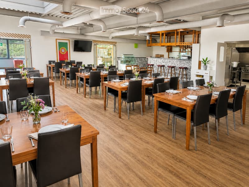 Restaurant interior with wooden tables, black chairs, and neatly set place settings, including plates, cutlery, and glassware. A bar area with stools and a television is visible in the background.