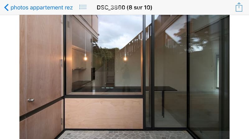 Modern hallway with large glass doors leading to a kitchen area, wooden cabinets, and pendant lights visible through the glass.