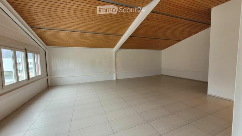 Empty room with white tiled floor, white walls, and wooden slatted ceiling. Three windows on one side provide natural light.