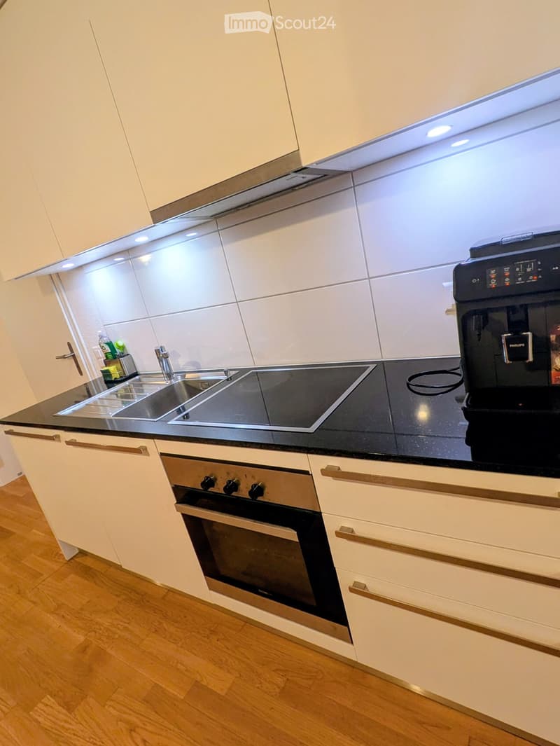 Modern kitchen with white cabinets, black countertops, stainless steel sink, induction cooktop, oven, and coffee machine.