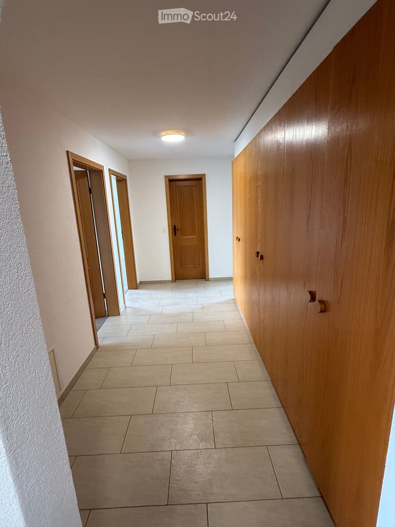 Empty hallway with tiled floor, wooden doors, and built-in wooden cabinetry on one side.