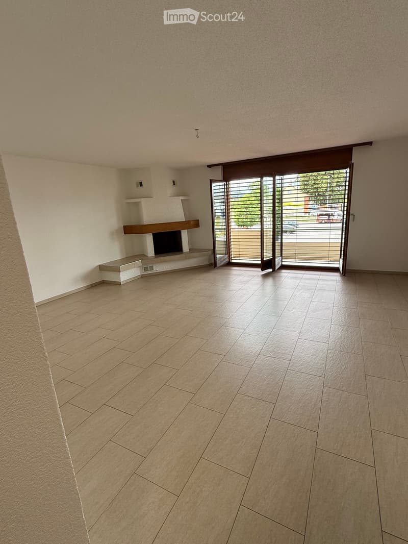 Empty room with beige tiled floor, white walls, and a fireplace with a wooden mantel. Large sliding glass doors lead outside.