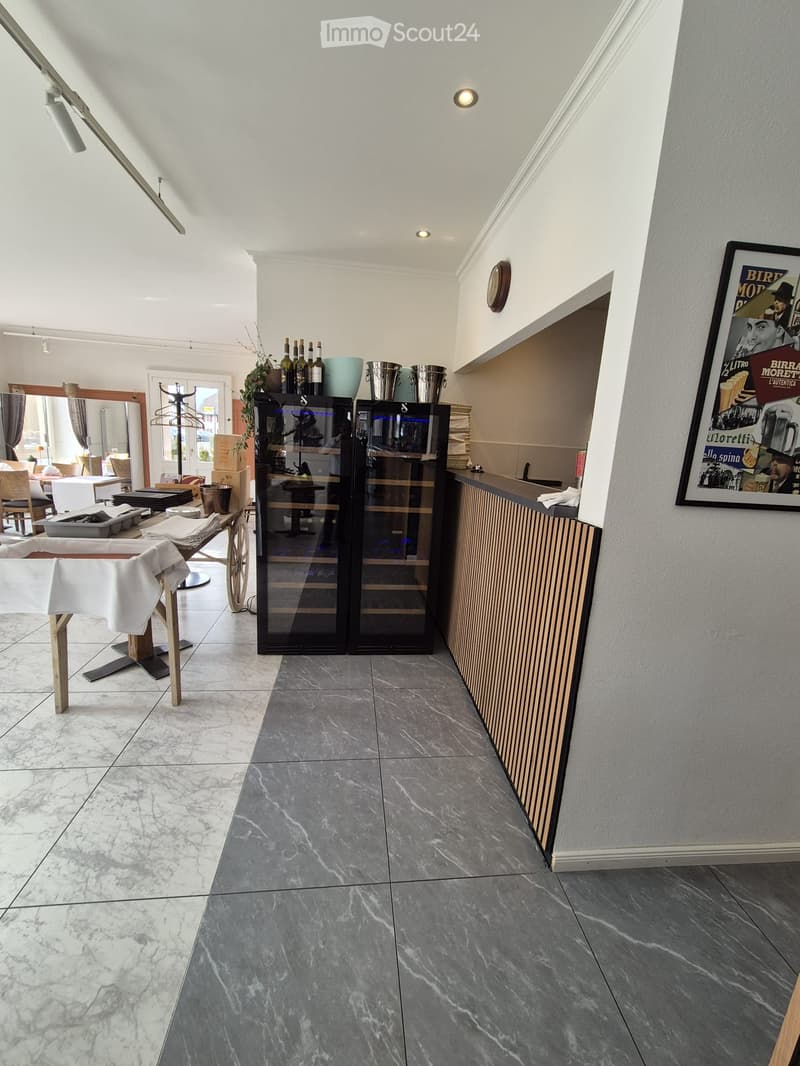 A modern, well-lit room with a mix of marble and grey tiles, featuring a wine cabinet, a small table with chairs, a mirror, and a framed poster on the wall.