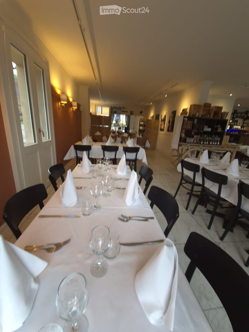 Restaurant dining area with multiple tables set for guests, each with wine glasses, cutlery, and napkins, surrounded by black chairs.
