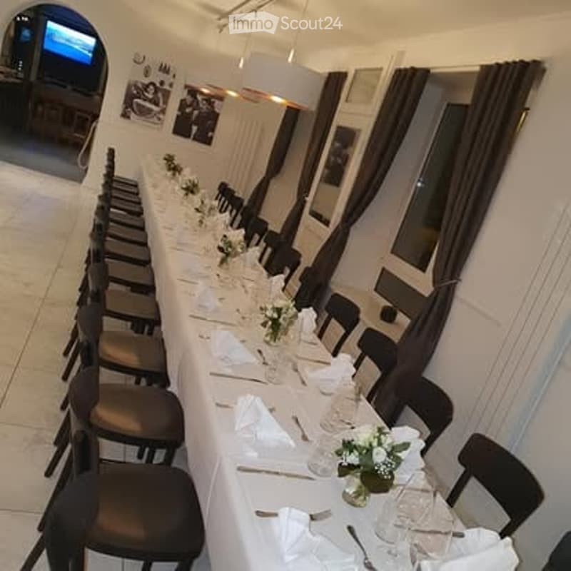 A long dining table set for a formal event, with white tablecloths, floral centerpieces, and neatly arranged silverware and glassware. Black chairs line both sides of the table.