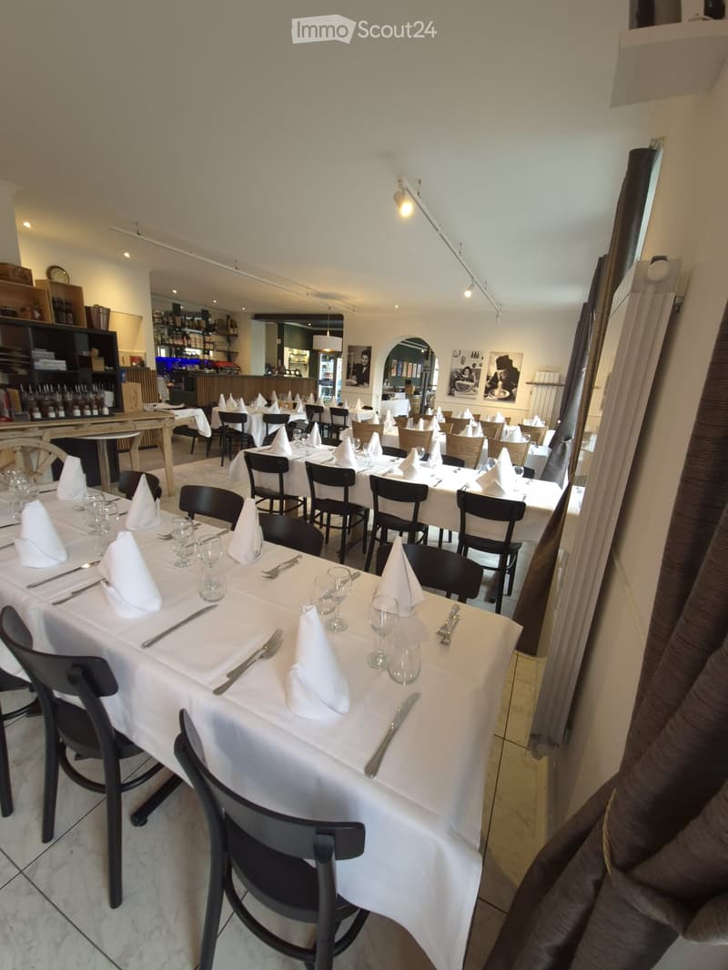 Restaurant dining area with multiple tables set for dining, each with white tablecloths, napkins, glasses, and cutlery, surrounded by black chairs.