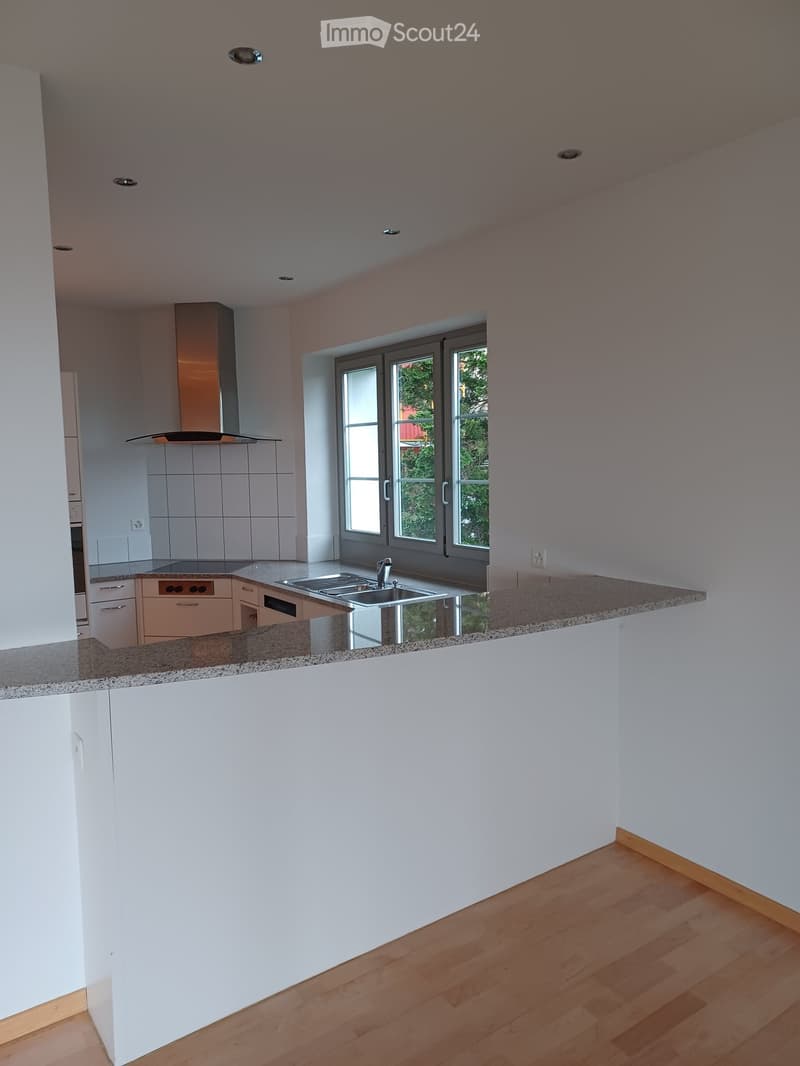 Modern kitchen with white cabinets, granite countertops, stainless steel sink, and a large window overlooking greenery.