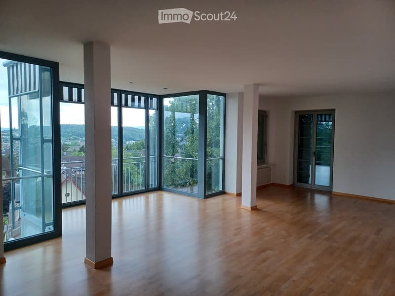 Empty room with wooden flooring, large windows, and a central column. No furniture or equipment present.