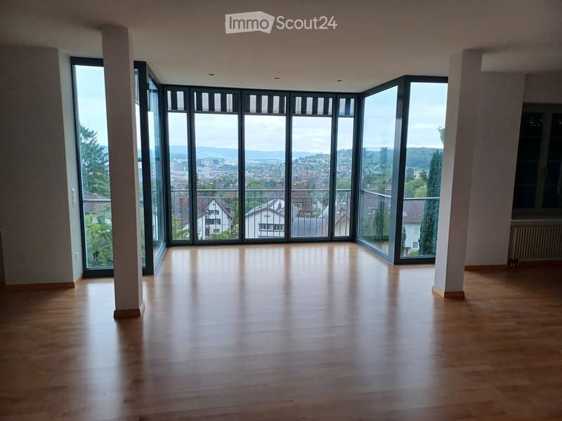 Empty room with wooden flooring, large windows offering a city view, and a balcony accessible through the windows.