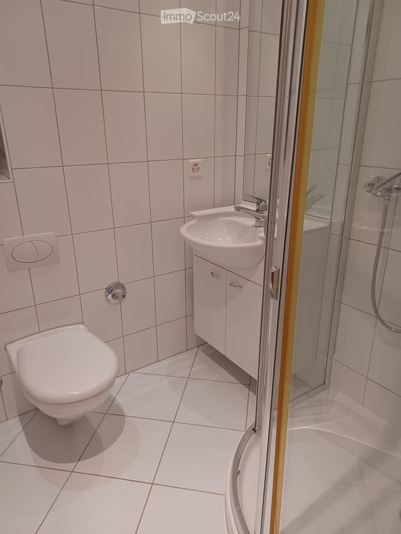 Modern bathroom with white tiles, a toilet, a sink with a cabinet, and a bathtub enclosed by a glass shower door.