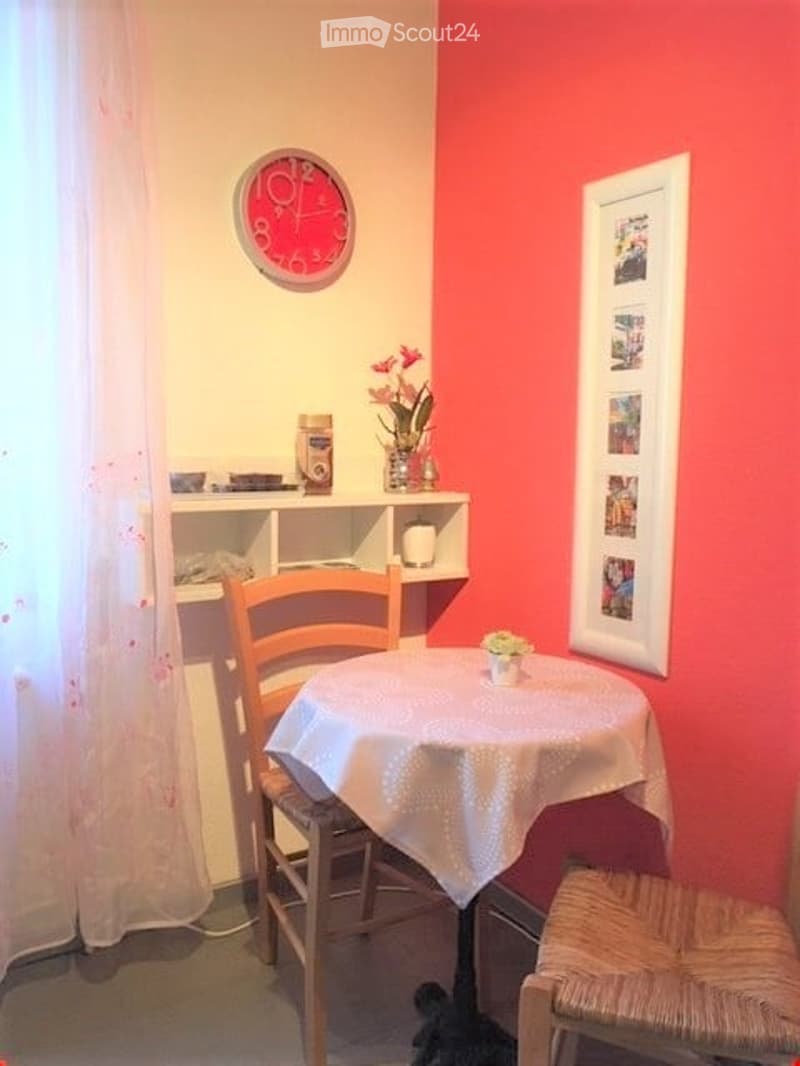 small dining area with a table and two chairs, a shelf with flowers and a clock on the wall