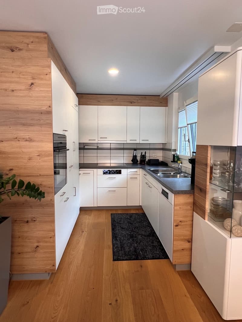 Modern kitchen with white cabinets, wooden accents, stainless steel appliances, and a central island.