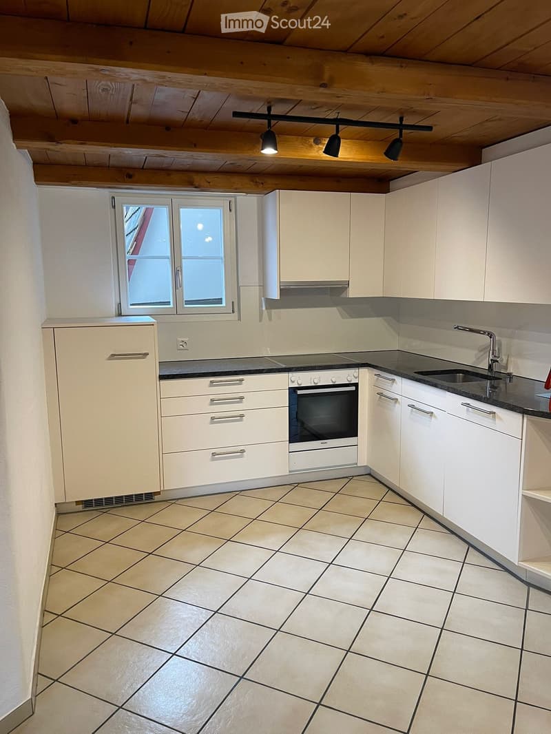 Modern kitchen with white cabinets, tiled floor, built-in oven, sink, and window.