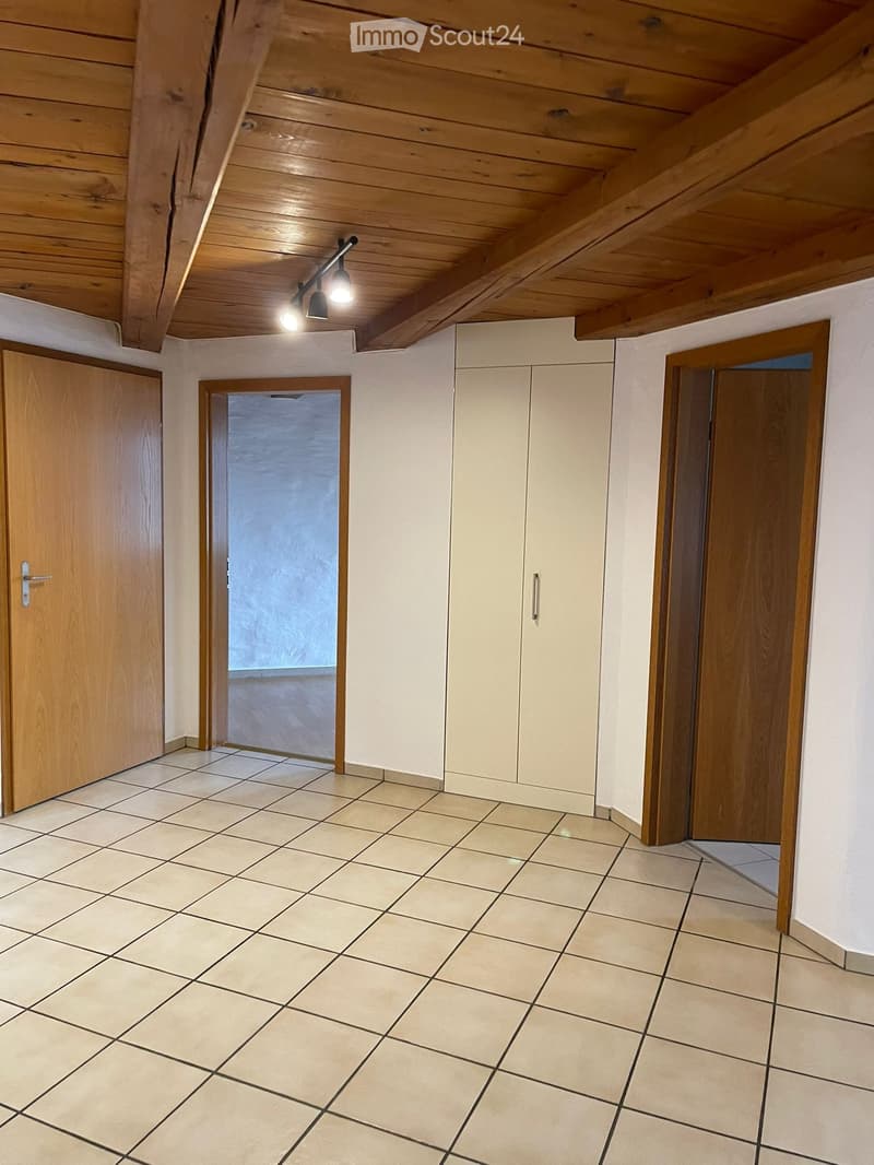 Empty room with tiled floor, white walls, wooden ceiling beams, and built-in cabinets. Three doors lead to other spaces.