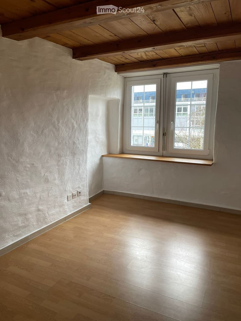 Empty room with wooden flooring, white walls, and large windows with a wooden sill. Exposed wooden beams on the ceiling.