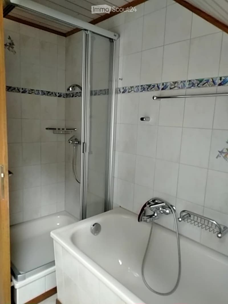 Bathroom with a white bathtub, a glass-enclosed shower, and tiled walls. Features include a faucet, shower handle, and a towel rack.