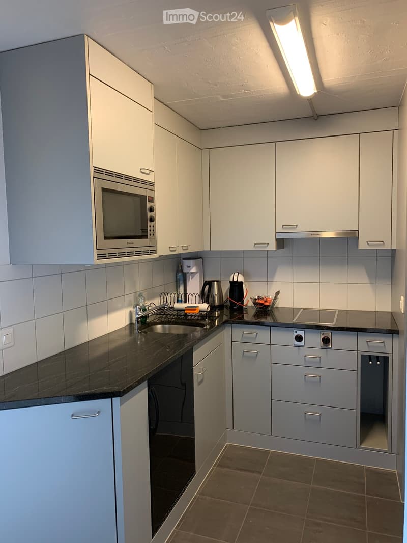 Modern kitchen with white cabinets, black countertops, stainless steel appliances, and a built-in microwave. Includes a sink, coffee maker, and various small items on the counter.