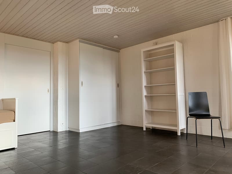 Minimalist room with dark tiled floor, white walls, a black chair, a white shelf, and a large wardrobe.