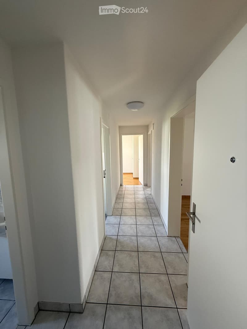 Empty hallway with tiled floor, white walls, and several doors leading to other rooms.