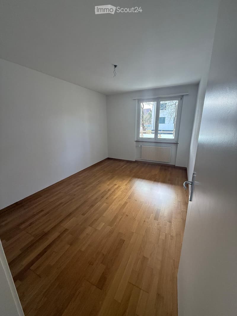Empty room with wooden flooring, white walls, and a window with a radiator below it. No furniture or equipment is present.
