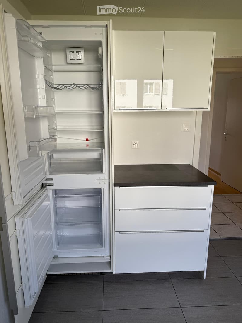 Modern kitchen with white cabinets, a black countertop, and an open refrigerator with multiple compartments.