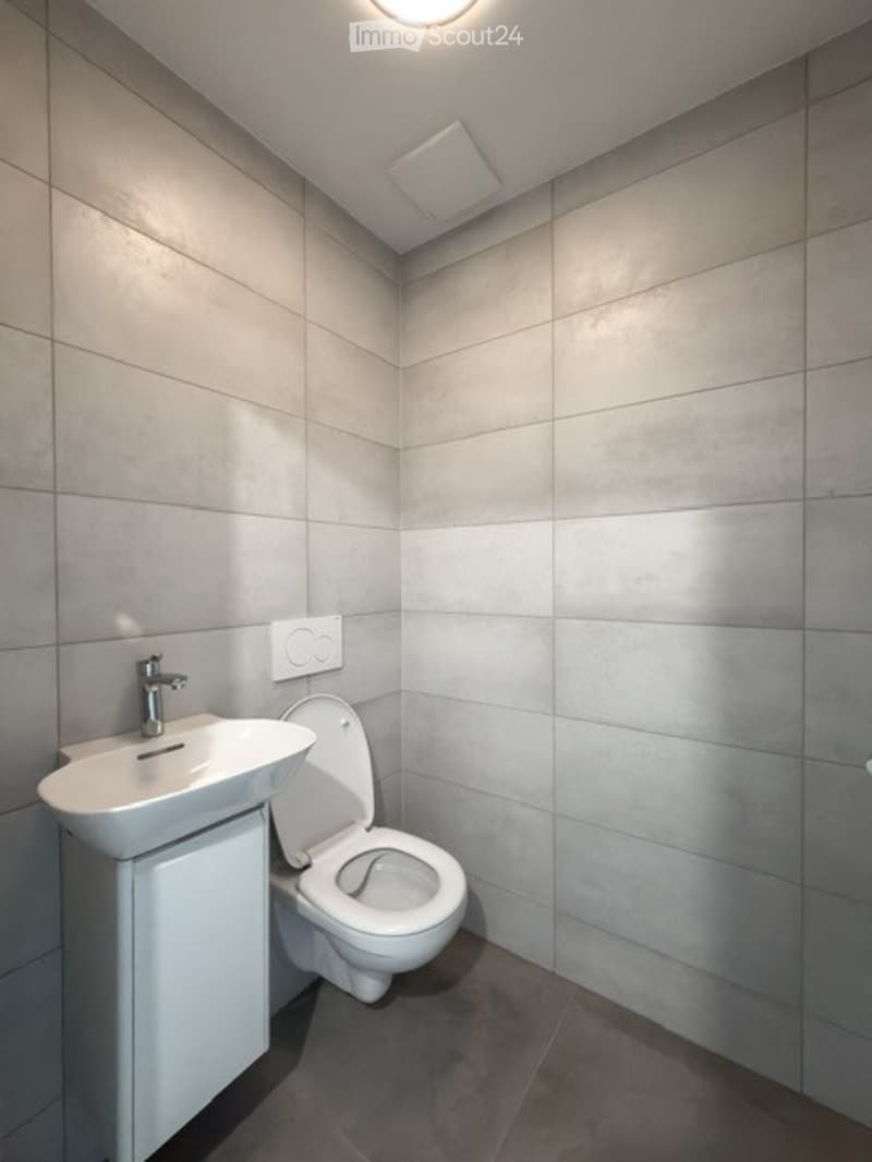Modern bathroom with grey tiled walls and floor, white sink with chrome faucet, and white toilet.