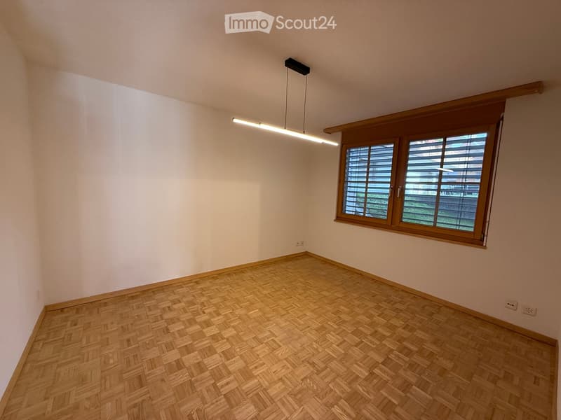 empty room, white walls, wooden parquet flooring, two white outlets, a window with wooden shutters, a ceiling lamp