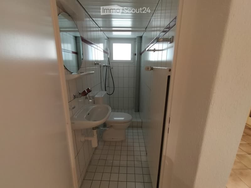 small bathroom with toilet, sink, mirror, white tiled floor, small window, shower area
