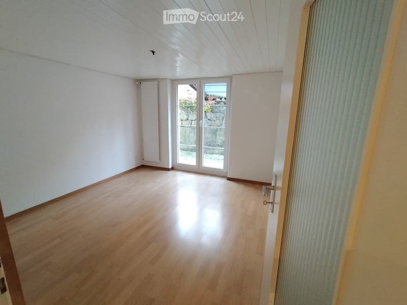 Empty room with wooden floor, white walls, large windows, sliding door