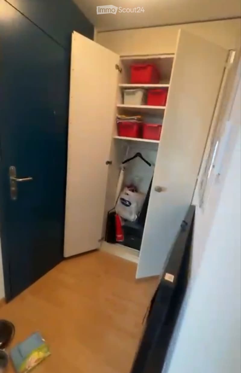 Empty room with wooden flooring, white built-in closet with shelves, and a dark blue door.
