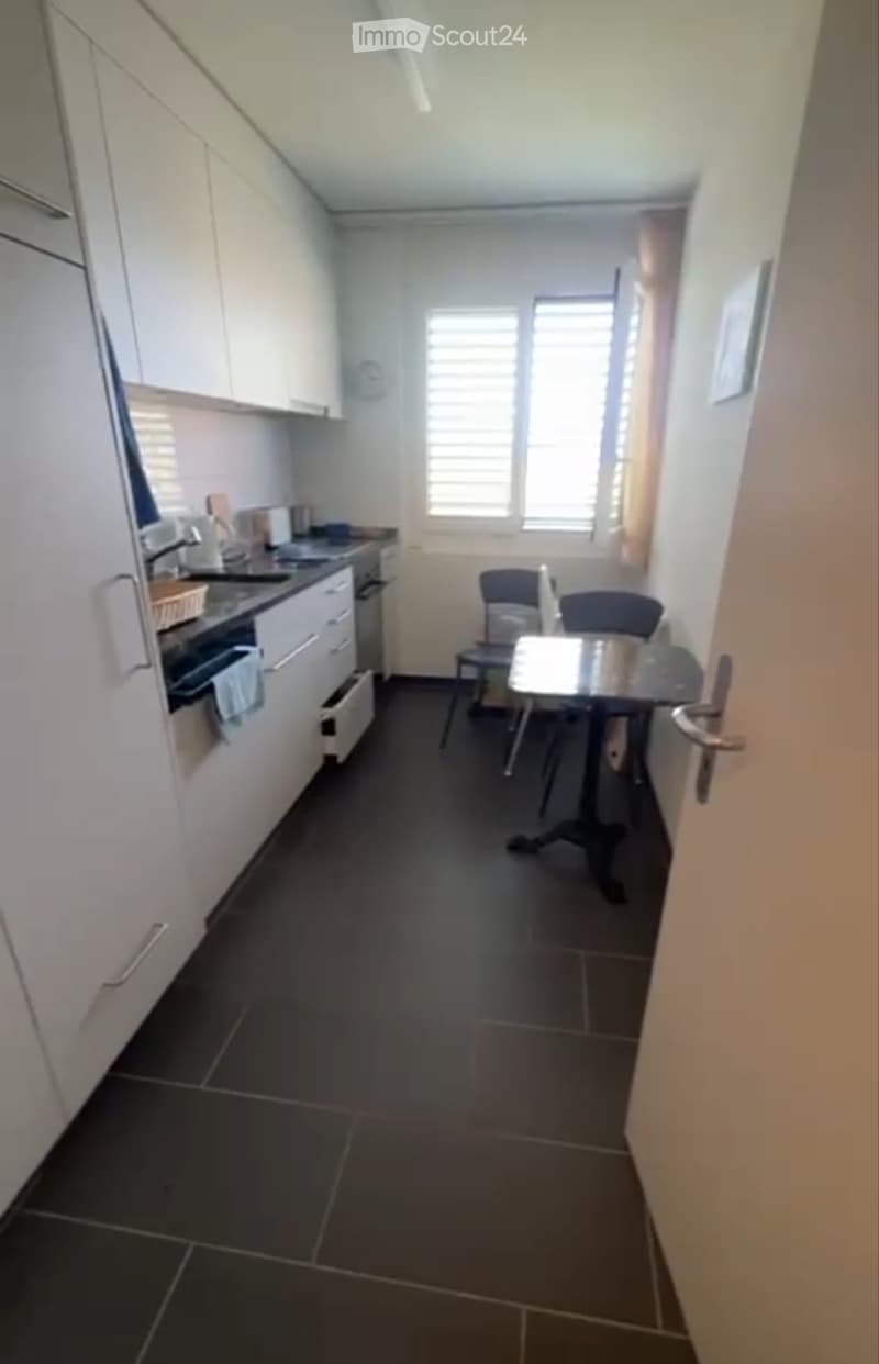 Modern kitchen with white cabinets, dark tiled floor, and a small dining area with a table and chairs.