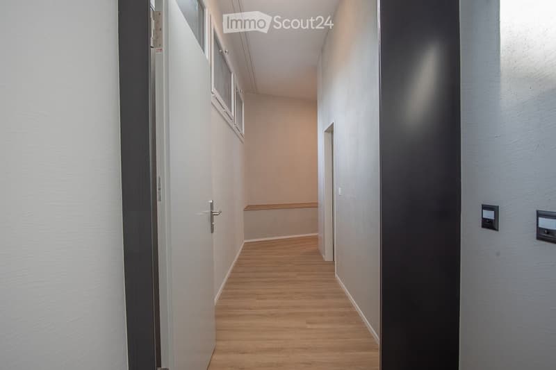 Empty hallway with wooden flooring, white walls, two doors, and windows.