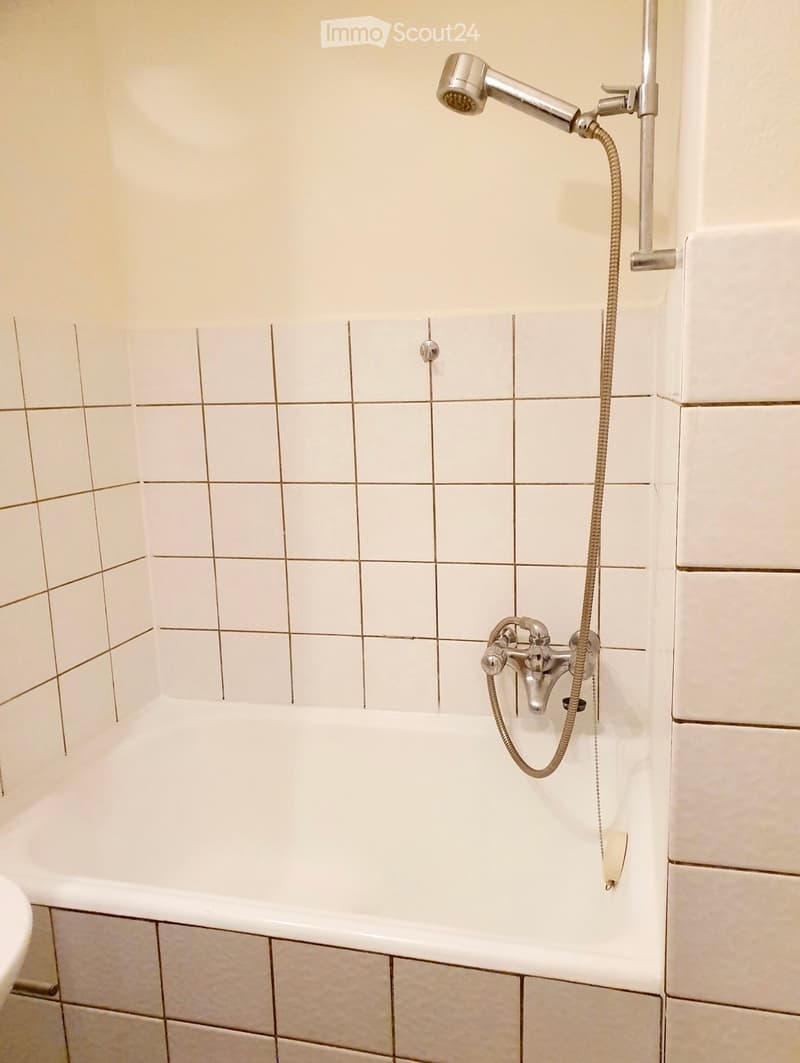 Bathtub with a handheld showerhead and faucet, tiled walls and floor.