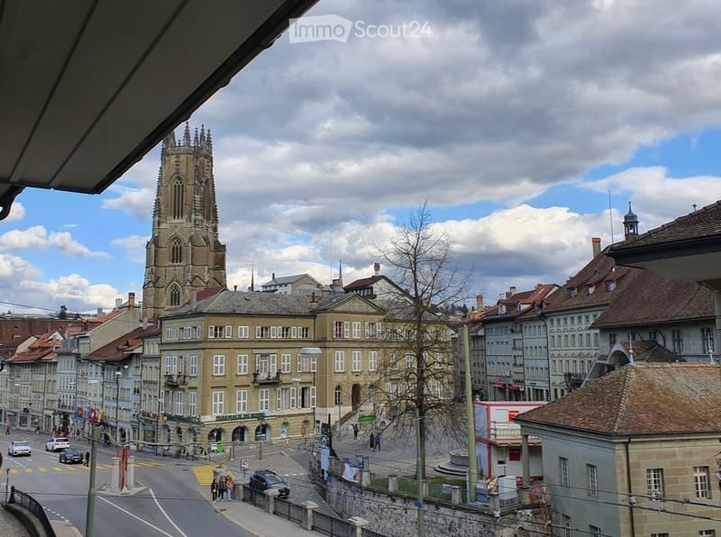 Balcony view of a historic cityscape with a prominent church tower, traditional buildings, and a busy street below.