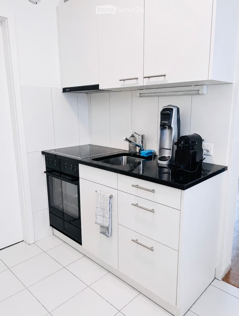 Modern kitchen with white cabinets, black countertop, stainless steel sink, oven, coffee maker, and a towel hanging from a cabinet handle.