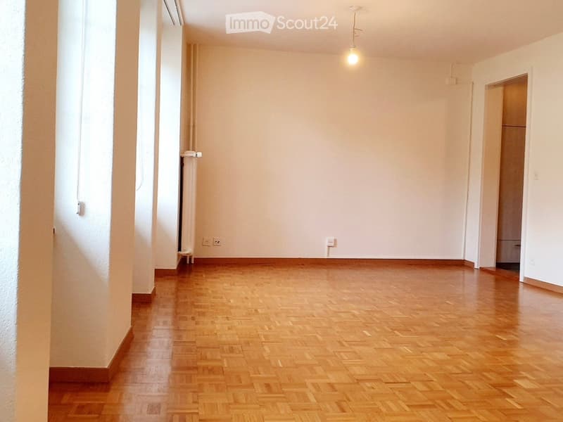 Empty room with wooden parquet flooring, white walls, and a single hanging light fixture.