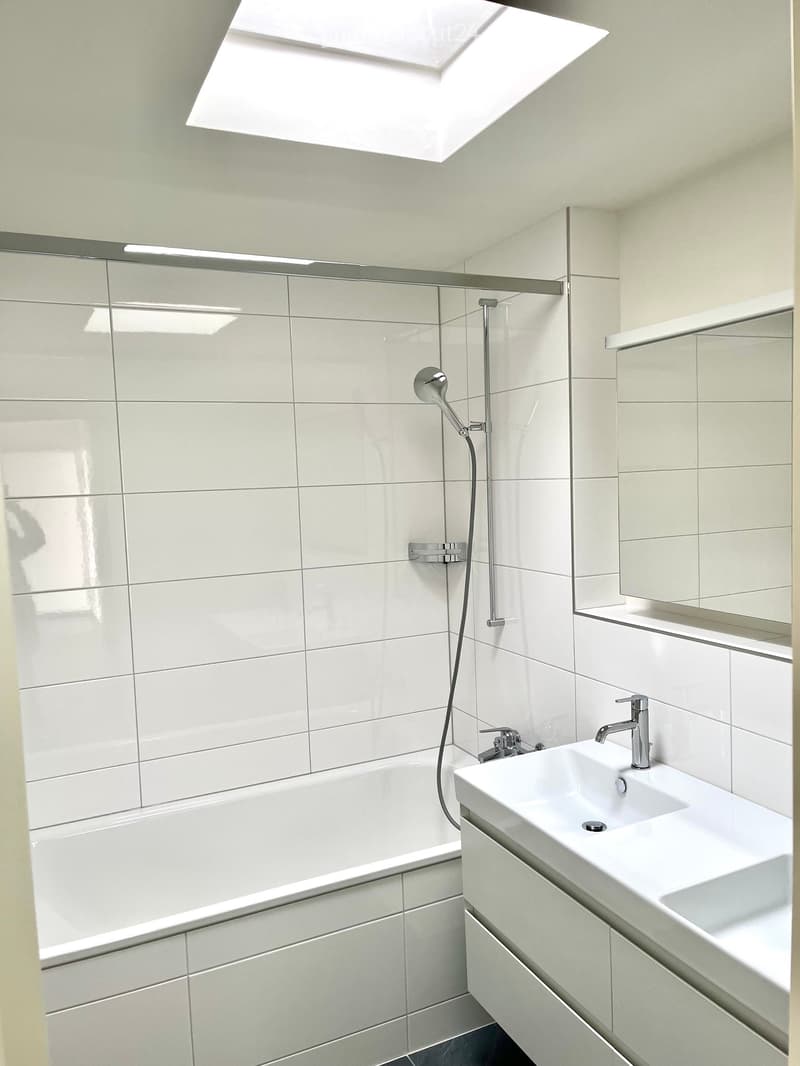 Modern bathroom with white tiles, a bathtub, a sink with a modern faucet, and a showerhead with a handheld sprayer.