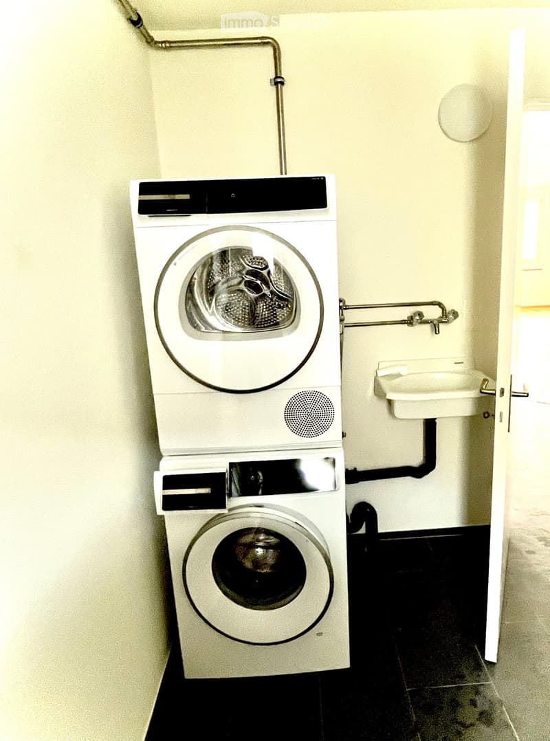 Bathroom with a stacked washing machine and dryer unit, a small sink, and a window providing natural light.