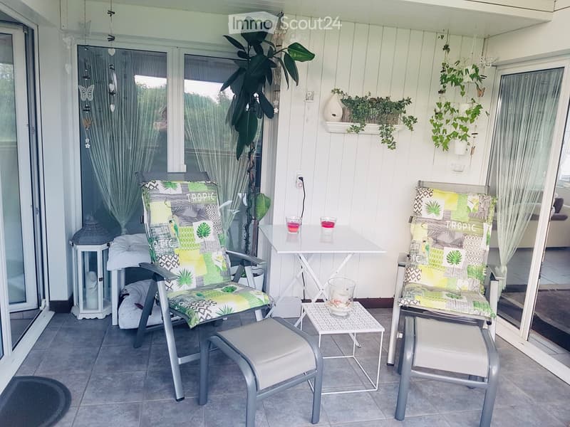 Balcony with two chairs, a small table, a stool, a lantern, and decorative plants.