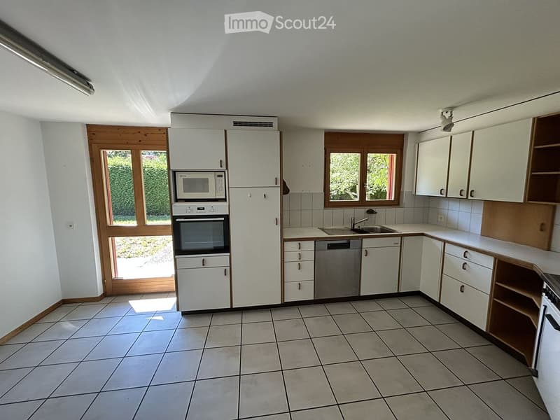 Bright, modern kitchen with white cabinets, tiled floor, microwave, oven, dishwasher, and sink. Large windows provide natural light.