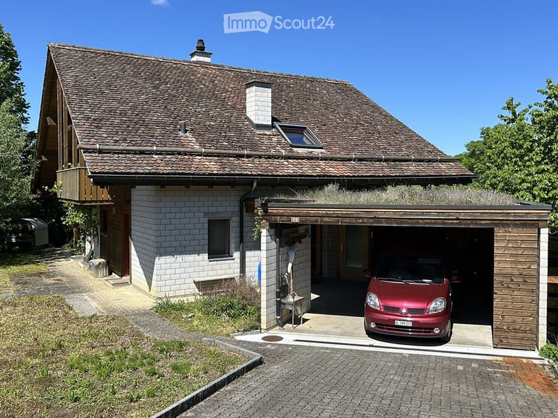 Two-story house with a tiled roof, white brick lower level, and wooden upper level. Features a covered garage with a red car parked inside.