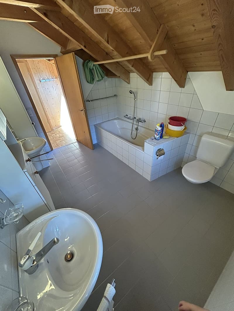 Bathroom with a sink, toilet, bathtub, and a mirror. The room has tiled walls and a wooden ceiling with exposed beams.