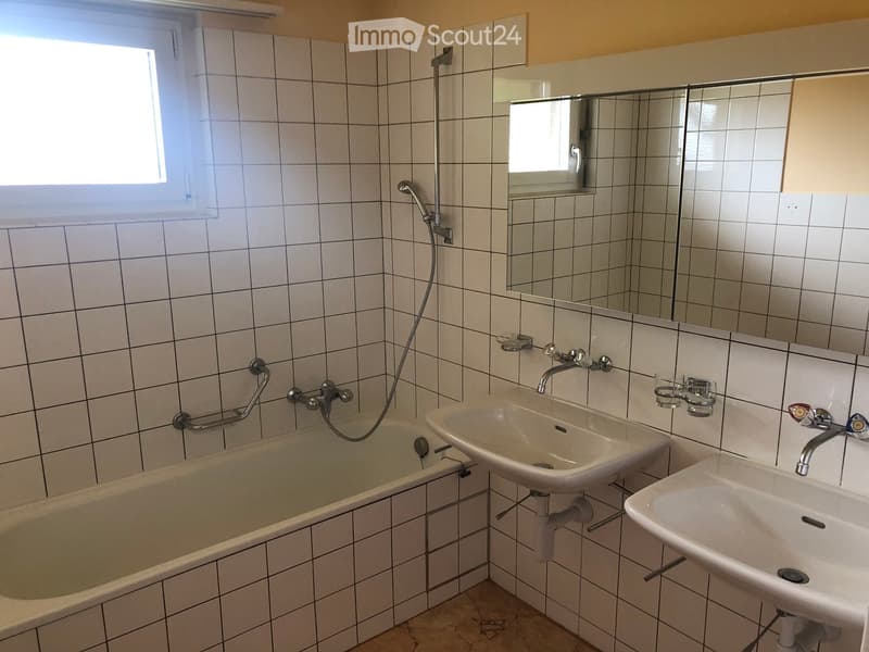 Bathroom with tiled walls, bathtub, two sinks, mirror, and handrail.