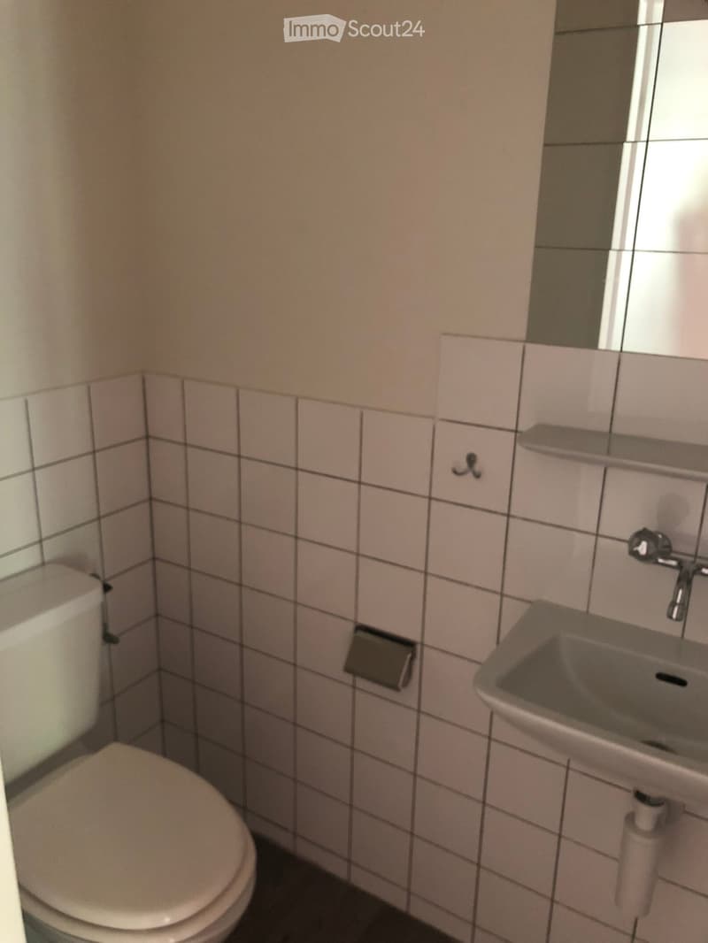 Small bathroom with white tiled walls, a toilet, a sink with a faucet, and a mirror above the sink.