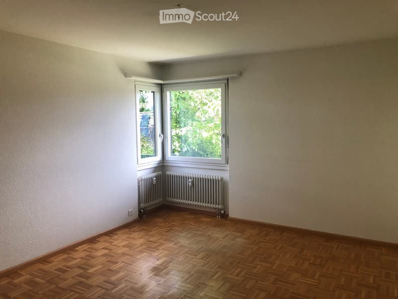 Empty room with wooden parquet flooring, white walls, and two windows with radiators below them.