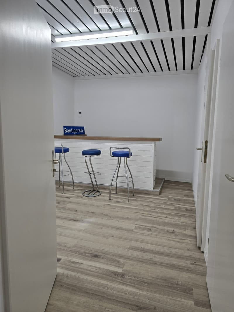 A small, modern bar area with three blue stools, a wooden counter, and a sign on top.
