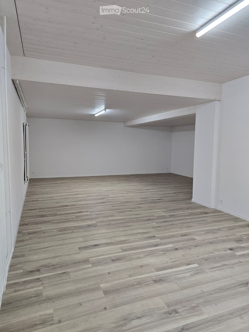 Empty room with wooden flooring and white walls, featuring exposed wooden beams on the ceiling and a small built-in shelf on one wall.