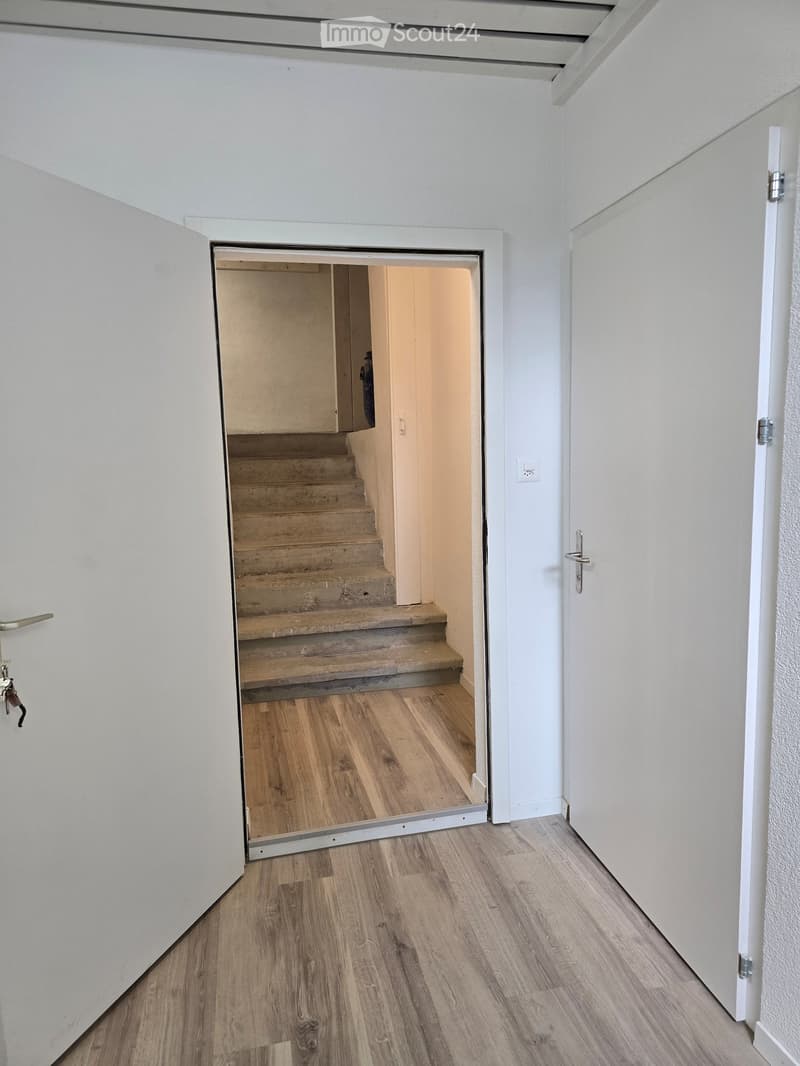 Empty hallway with wooden flooring, white walls, and a staircase leading upwards.